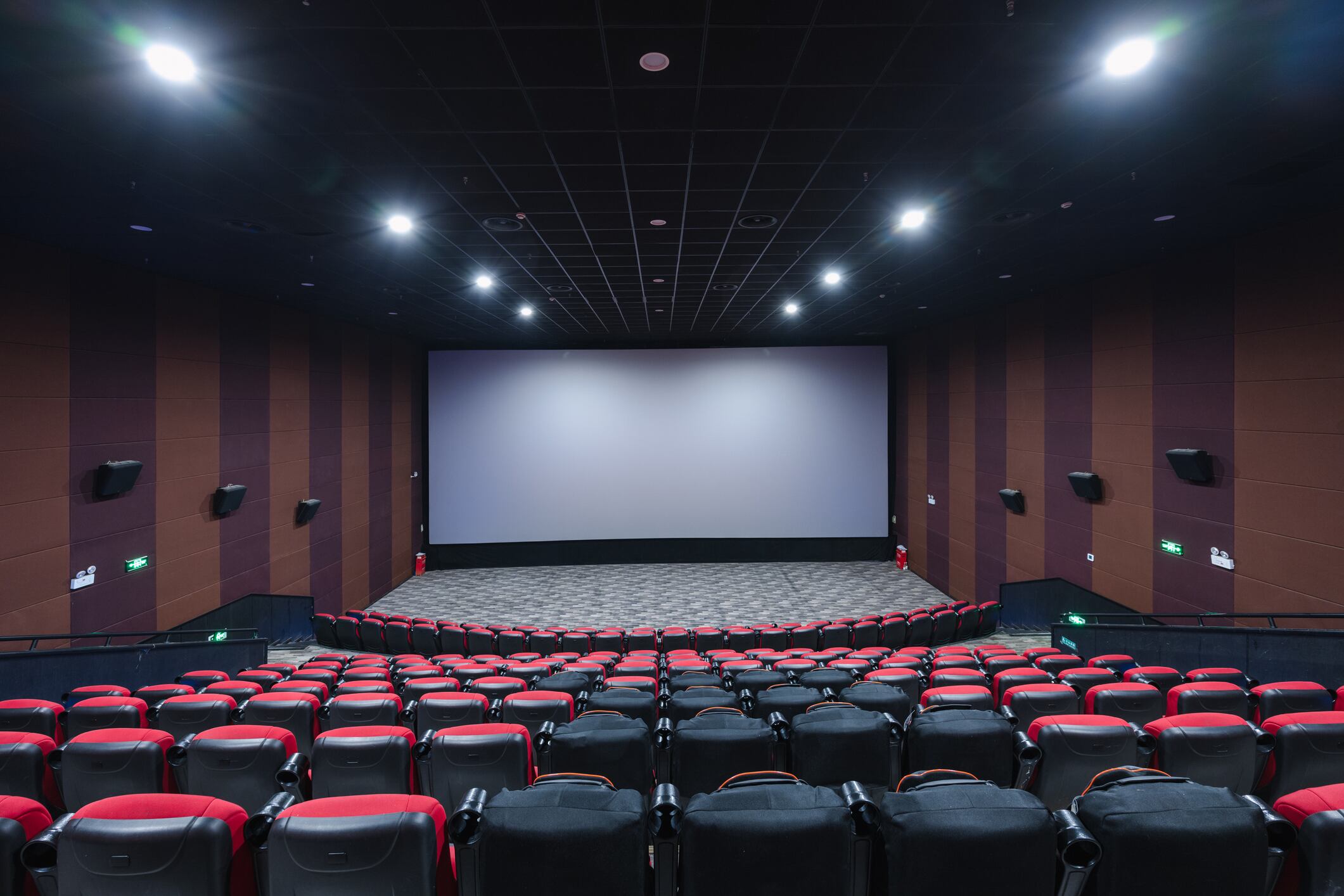 A huge laser-projected movie screening hall interior, red and black chairs neatly arranged, and comfortable massage chairs for moviegoers to choose from, providing them with a high-quality viewing experience.