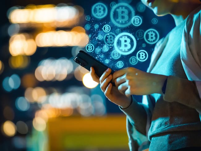 Mid-section of young Asian woman using smartphone in city at night, against illuminated street lights bokeh, working with Bitcoin technologies, investing or trading Bitcoin on cryptocurrency. Business on the go