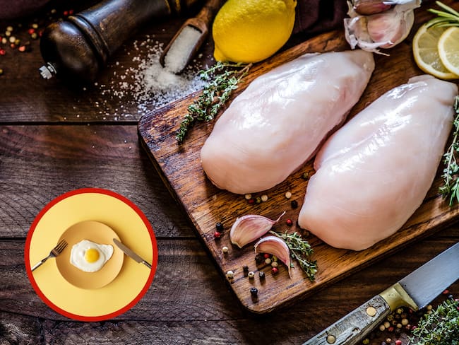 Pollo crudo sobre una tabla junto a un huevo frito sobre un plato (Foto vía Getty Images)