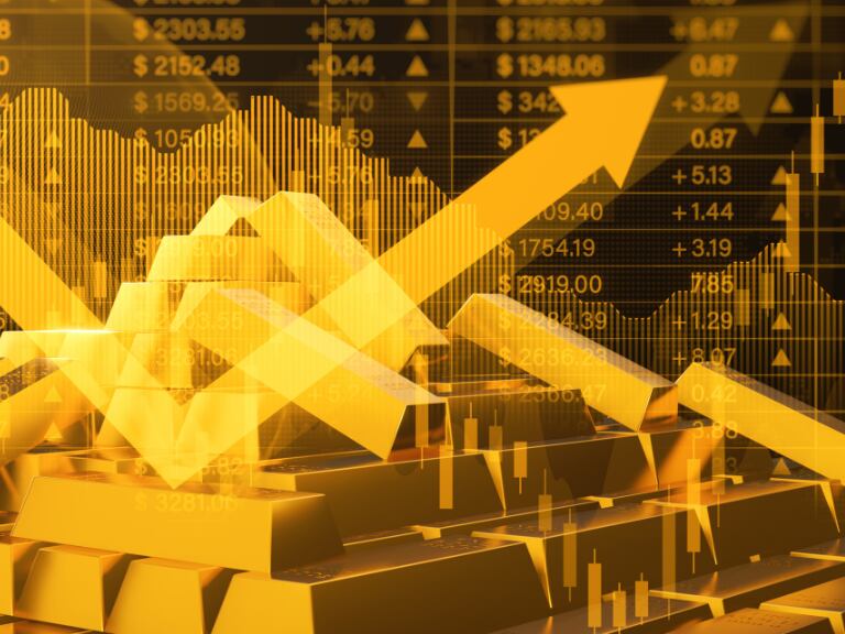 Lingotes de oro con una ilustración de la fluctuación de cifras al fondo (Foto vía Getty Images)