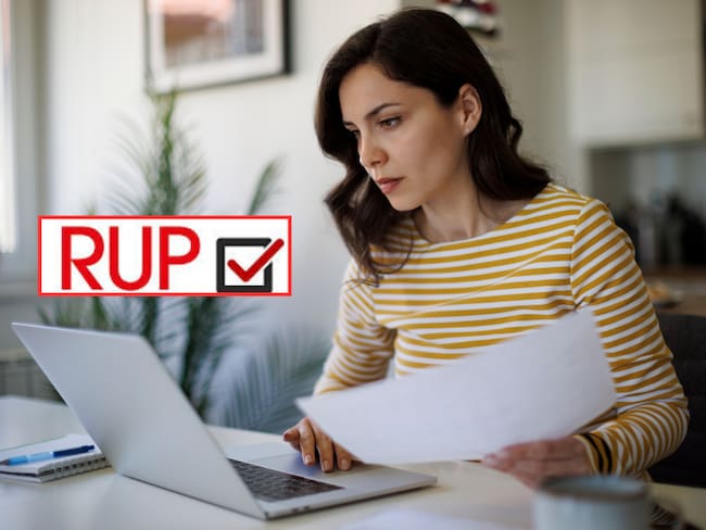 Persona revisando su computador con documento en su mano (Getty Images)