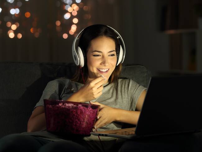Mujer viendo películas en su computador y comiendo palomitas de maíz (Foto vía Getty Images)