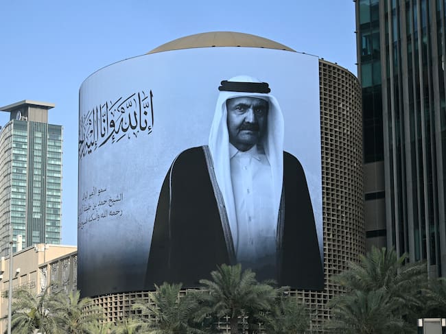 A photograph shows a billboard bearing a portrait of Qatar's former leader Sheikh Hamad bin Khalifa Al Thani in Doha on July 12, 2026, after the announcement of his death. The former leader was seen as one of the key architects of modern Qatar and led the country during a period of rapid economic growth. He took power in June 1995, overthrowing his father in a bloodless coup while the latter was abroad. In June 2013, he surprised many by voluntarily abdicating in favour of his son, Sheikh Tamim, a first in the recent history of the Arab world. (Photo by Mahmud HAMS / AFP)