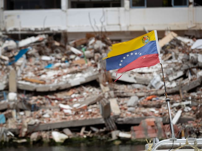 Fotografía de una bandera de Venezuela frente a un edificio colapsado por los terremotos del 24 junio, en La Guaira (Venezuela). EFE/ Ronald Peña R
