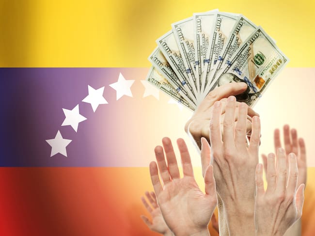 People raising hands with dollars and flag Venezuela on background. (Credito: JNemchinova // Getty imagenes)