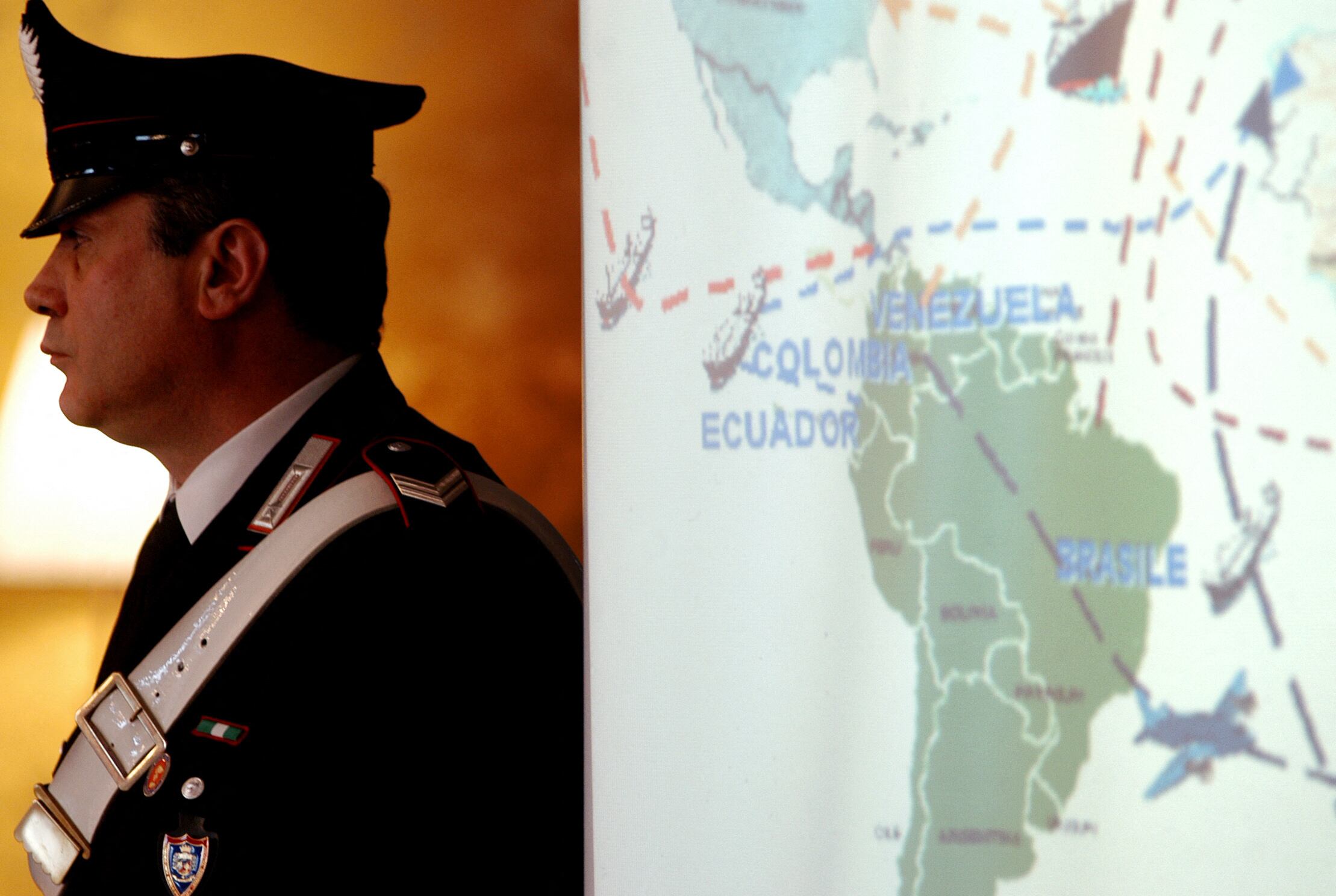 An Italian Carabiniere stands next to a slide-show illustrating the " Decollo" international anti-drugs operation during a news conference at a Rome's Carabinieri headquarter 28 January 2004 in Rome. Italian police seized thousands of kilos of Colombian cocaine today in a massive international anti-drugs operation aimed at cracking a vast network run by Colombian cartels and the Calabrian mafia, officials said. The Italians, working with police in six other countries, Australia, Colombia, France, the Netherlands, Spain and Venezuela, issued some 100 arrest warrants here with another 40 issued abroad, they said. (Photo by Andreas SOLARO / AFP) (Photo by ANDREAS SOLARO/AFP via Getty Images)