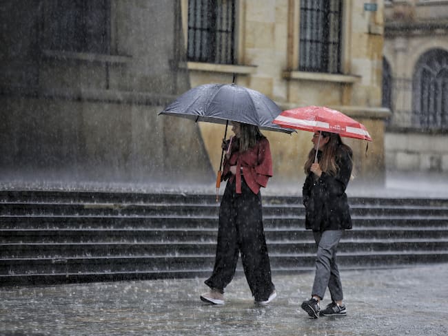 Mujeres caminando por el centro de Bogotá con sombrilla mientras llueve (Getty Images)