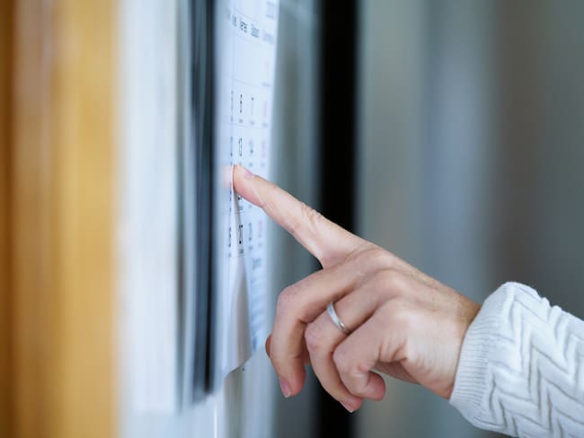 Mano de mujer señalando con su dedo el calendario pegado en la pared (Getty Images)