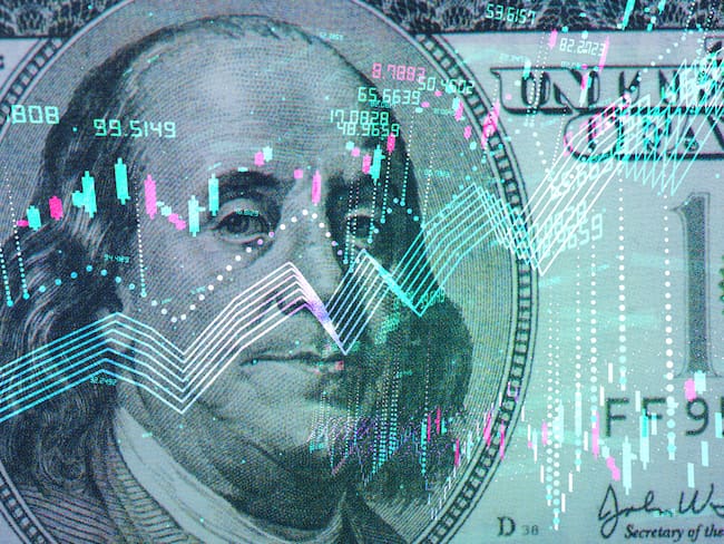 Billete de 100 dólares estadounidense con gráfico de indicadores económicos (Getty Images)