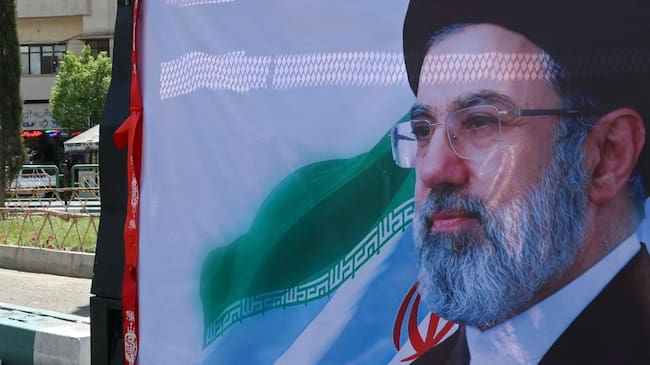 A man walks past a banner depicting Iran's new supreme leader Ayatollah Mojtaba Khamenei, along a street in Tehran on April 5, 2026. Oman and Iran held talks on easing passage through the Strait of Hormuz, the Omani state news agency reported on April 5, with the key shipping chokepoint effectively closed due to war in the Middle East. (Photo by AFP) /