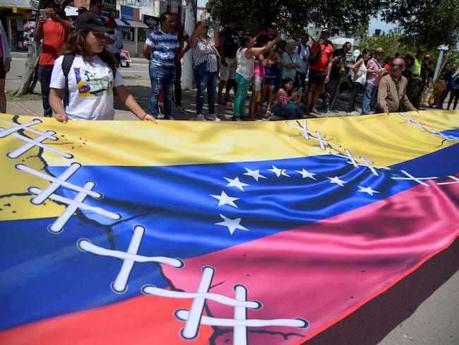 People display a banner showing Colombian and Venezuelan flags stitched to each other, as the land border between the two countries, completely closed since 2019, is officially reopened, at the Simon Bolivar International Bridge, in Cucuta, Colombia, on September 26, 2022. - Venezuela and Colombia on Monday reopened their border to goods vehicles following seven years of partial closure, including three years of full closure due to a political spat. Colombia President Gustavo Petro and representatives of the government of Venezuela leader Nicolas Maduro attended the ceremony. (Photo by Schneyder Mendoza / AFP) (Photo by SCHNEYDER MENDOZA/AFP via Getty Images)
