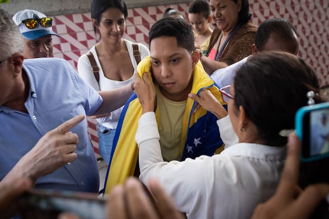AME6133. CARACAS (VENEZUELA), 23/12/2023.- Wendelin Peña (d) coloca una bandera venezolana sobre su hijo, el estudiante universitario John Álvarez (c), luego de salir en libertad de un centro de reclusión de la Policía Nacional Bolivariana (PNB) hoy, en Caracas (Venezuela). Las autoridades de Venezuela liberaron este sábado a Álvarez, preso desde el pasado 30 de agosto -acusado de conspiración y asociación para delinquir-, tras lo cual fue sometido a "torturas", según organizaciones de derechos humanos. El joven universitario, cuya salida del centro de detención fue corroborada por EFE, se une a la treintena de "presos políticos" que fueron puestos en libertad el pasado jueves, tras lo cual quedan, al menos, 265 personas privadas de la libertad por sus críticas al Ejecutivo, según los registros de varias ONG y de la coalición opositora Plataforma Unitaria Democrática (PUD). EFE/ Rayner Peña R.
