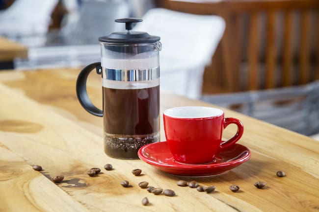 Prensa francesa, artefacto para preparar café sobre una mesa, al lado de una taza de cafpe de color rojo (Foto vía Getty Images)